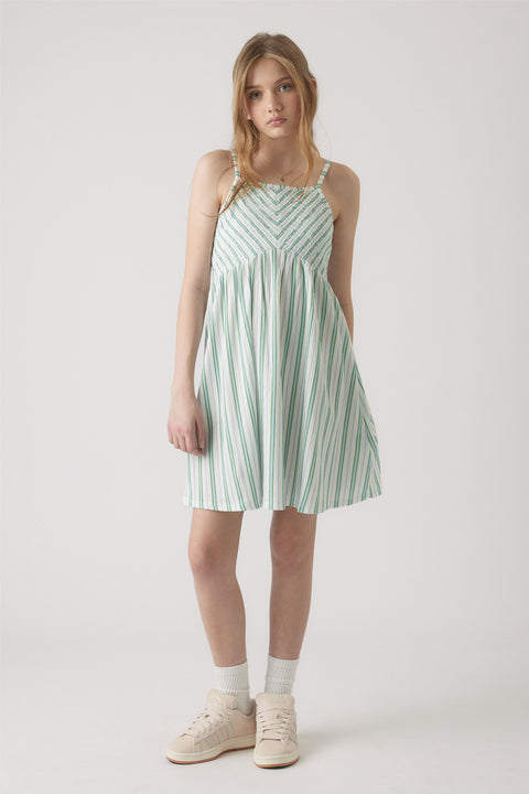 Girl wearing a white and green striped shirred dress with thin straps, paired with white socks and pale sneakers.