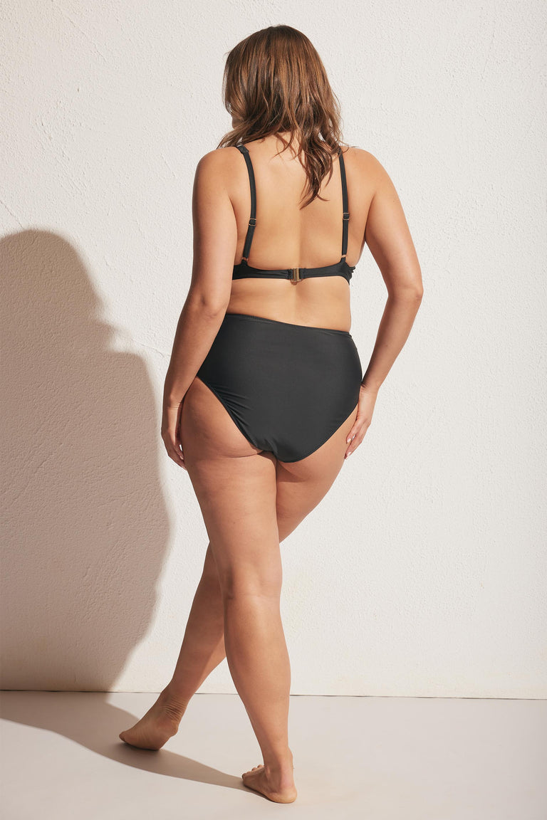 Woman modeling black matte gathered bikini bottom viewed from behind against textured wall