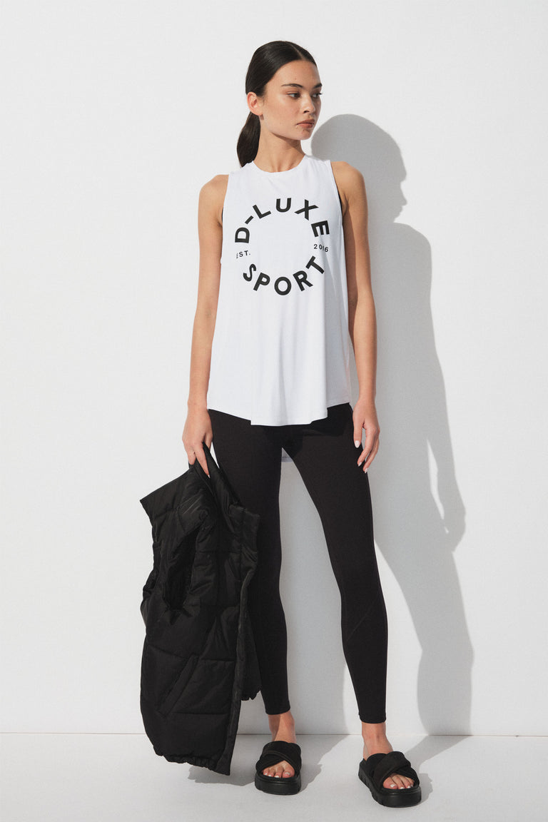 Woman wearing a white sleeveless tank with bold logo print paired with fitted black leggings and black slide sandals