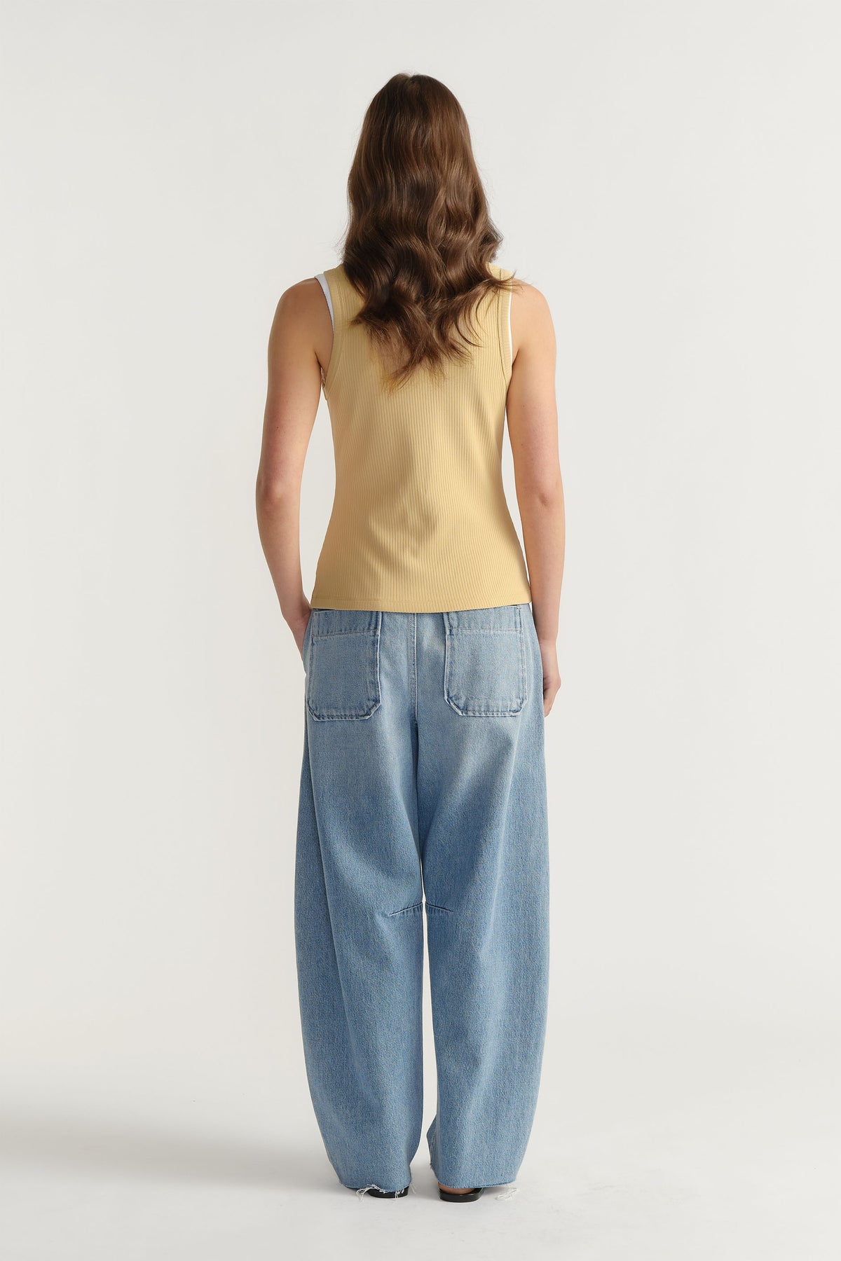 Woman wearing a beige ribbed tank paired with relaxed, wide-leg light blue denim jeans for a casual, effortless outfit.