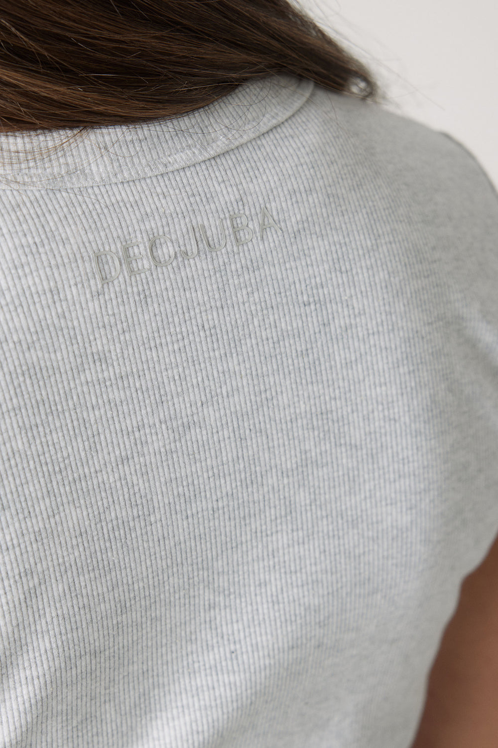 Close-up of a soft ice grey ribbed fabric crop tee featuring subtle embossed branding on the back neck.