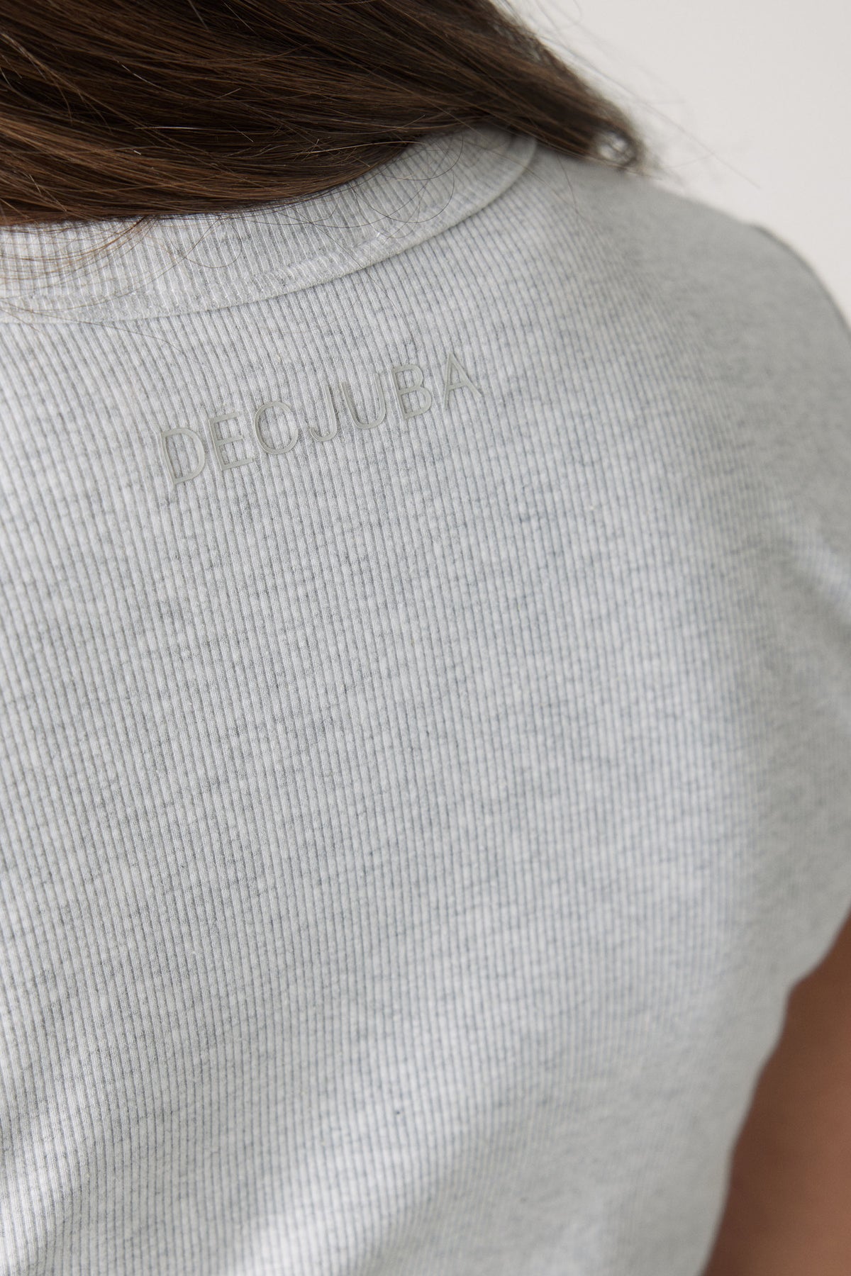 Close-up of a soft ice grey ribbed fabric crop tee featuring subtle embossed branding on the back neck.