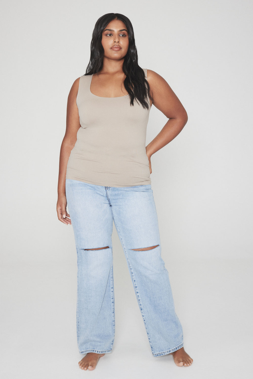 Woman wearing a beige scoop neck tank top and light blue ripped wide leg jeans
