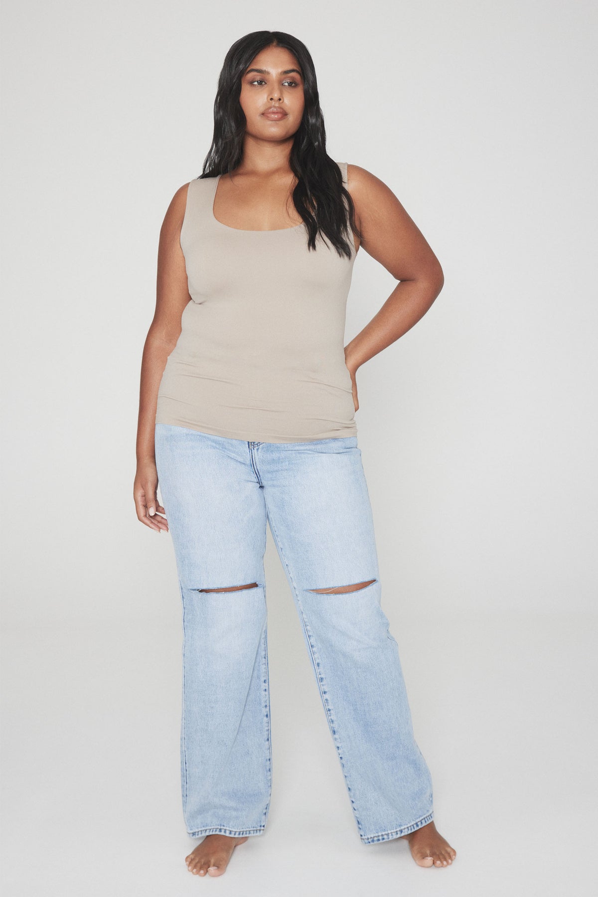 Woman wearing a beige scoop neck tank top and light blue ripped wide leg jeans