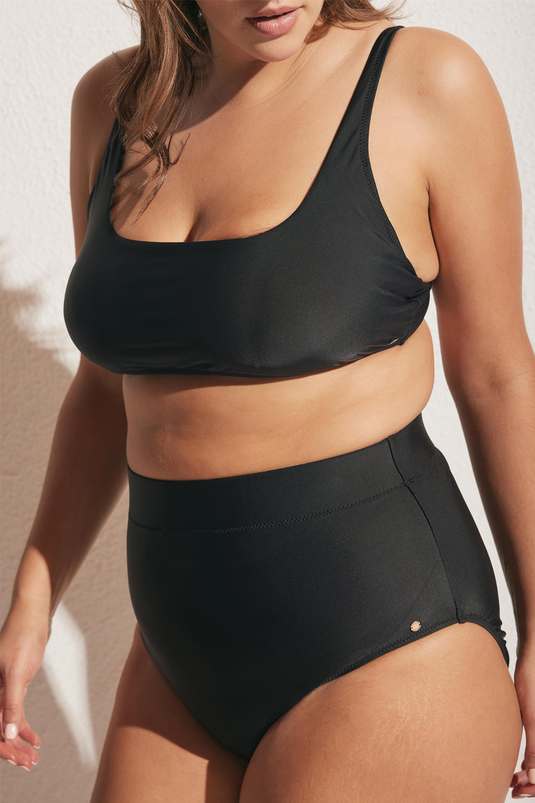 Woman wearing a black matte square neck bikini top with high-waisted matching bottoms in natural sunlight