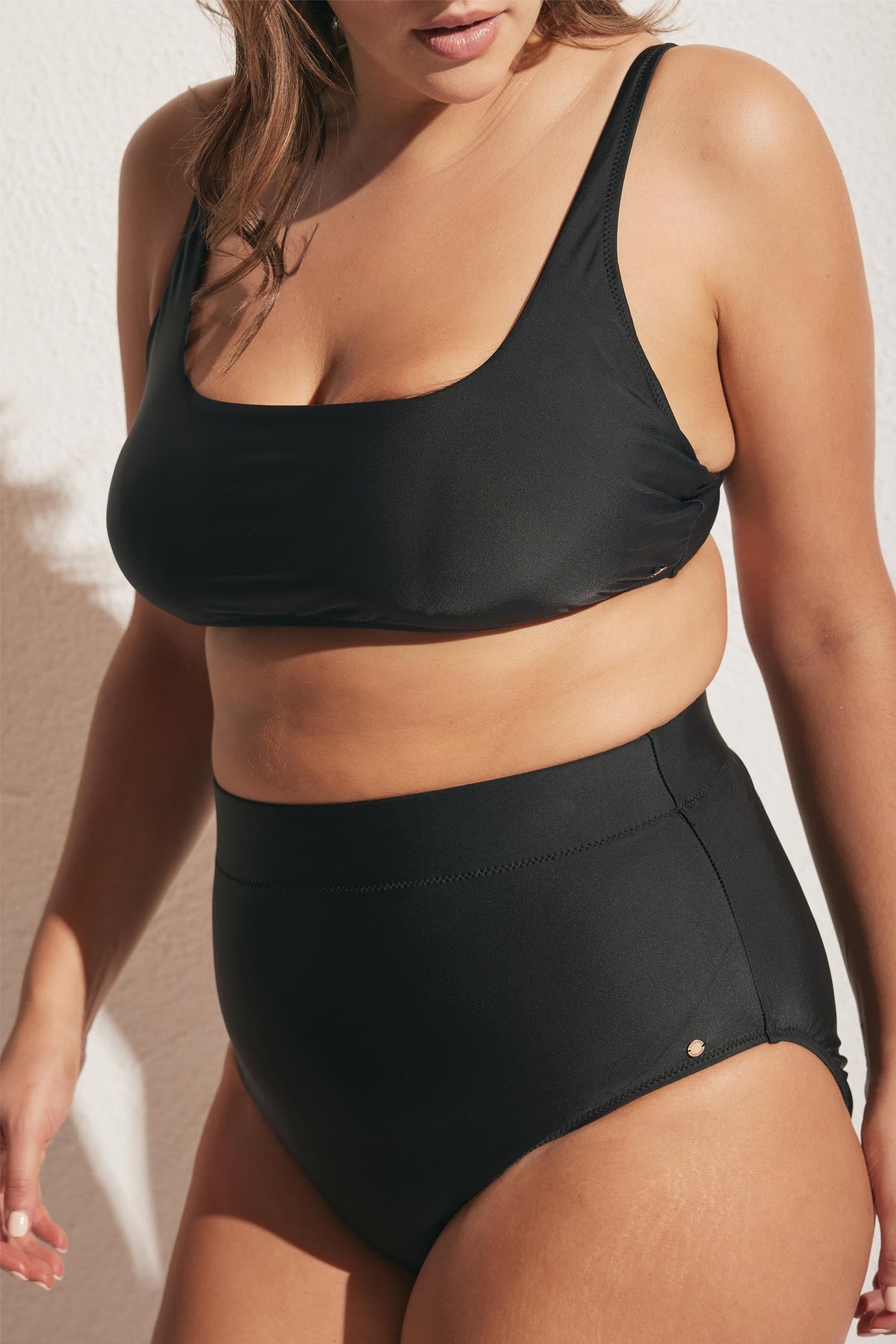 Woman wearing a sleek black high-waist bikini bottom paired with a matching simple bikini top in natural light