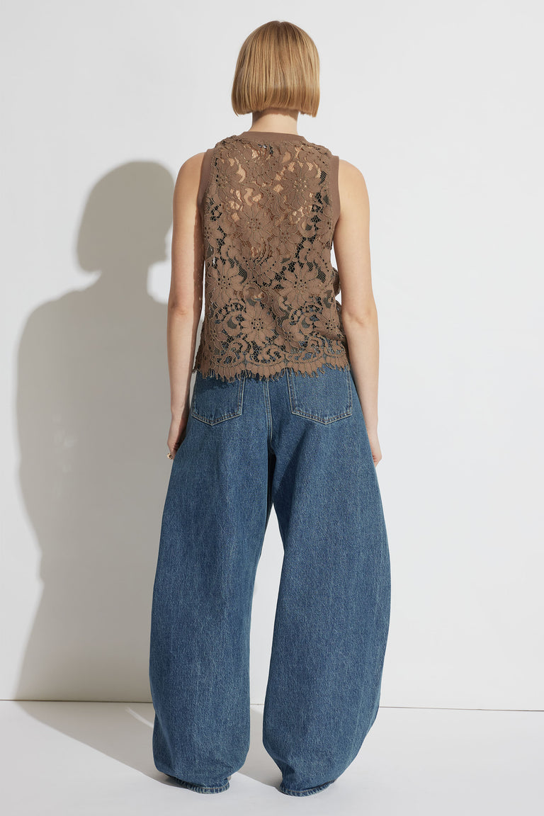 Woman wearing a cappuccino lace tank with floral pattern paired with wide-leg blue denim jeans standing against white background