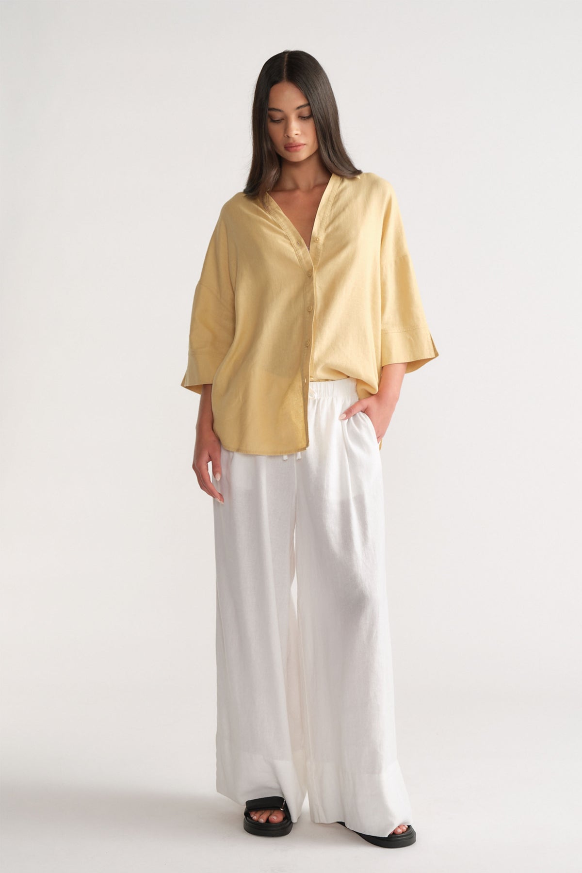 Portrait of a woman wearing the D-Luxe Linen Blend 3/4 Shirt in soft yellow, styled with white wide-leg pants