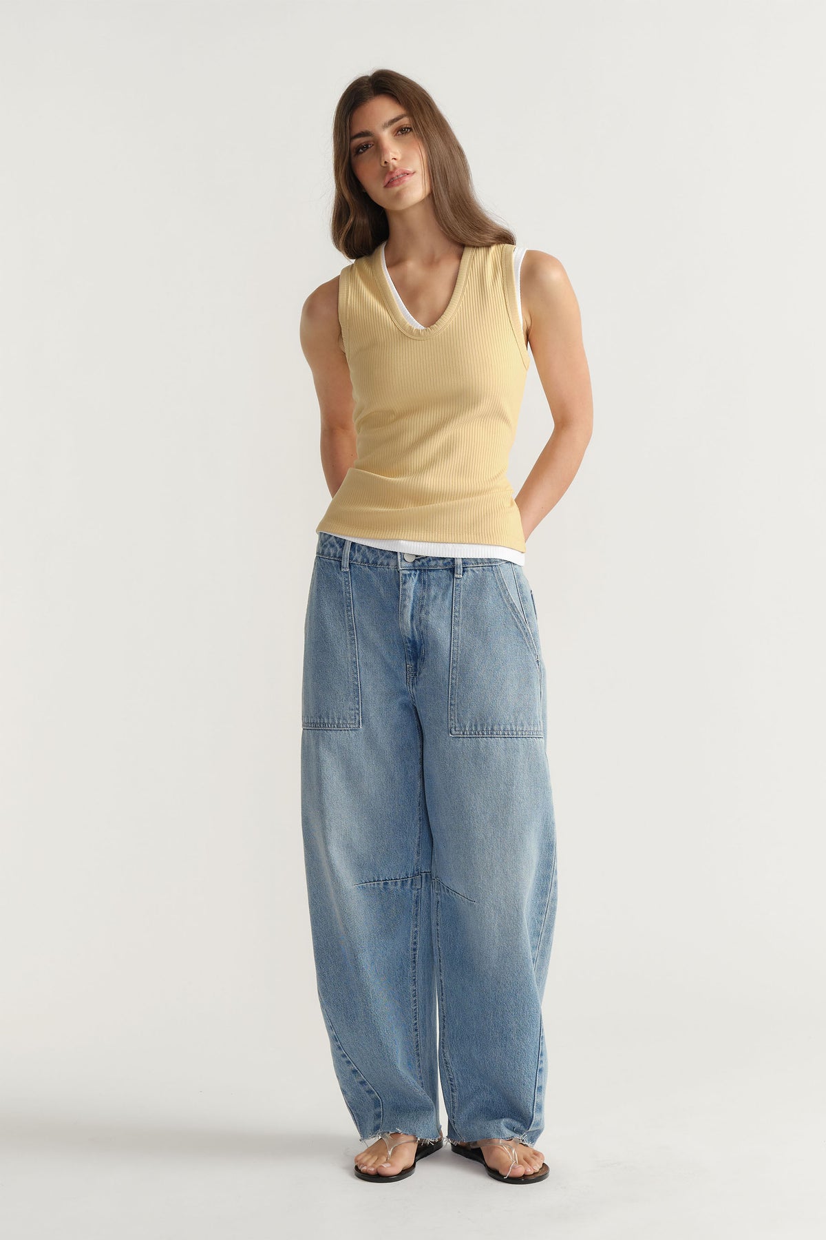 Woman wearing a soft yellow ribbed tank layered over white with loose light blue denim pants for a casual look