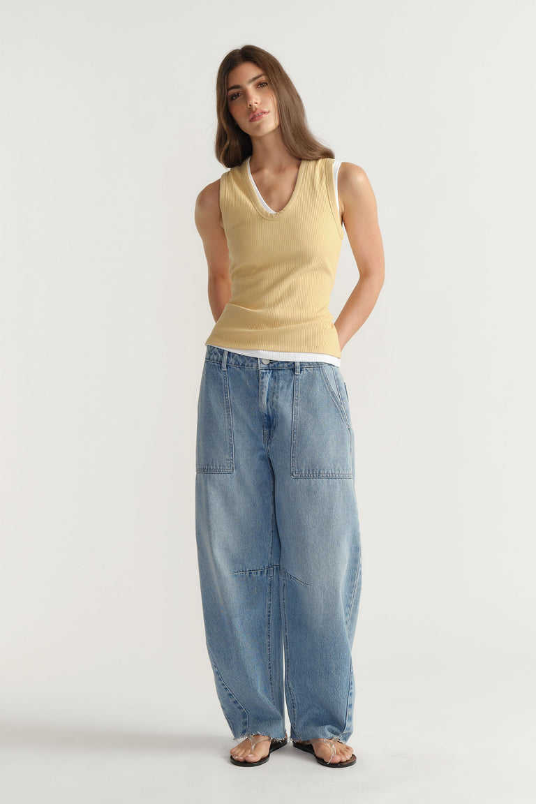 Woman wearing a soft yellow ribbed tank layered over white with loose light blue denim pants for a casual look