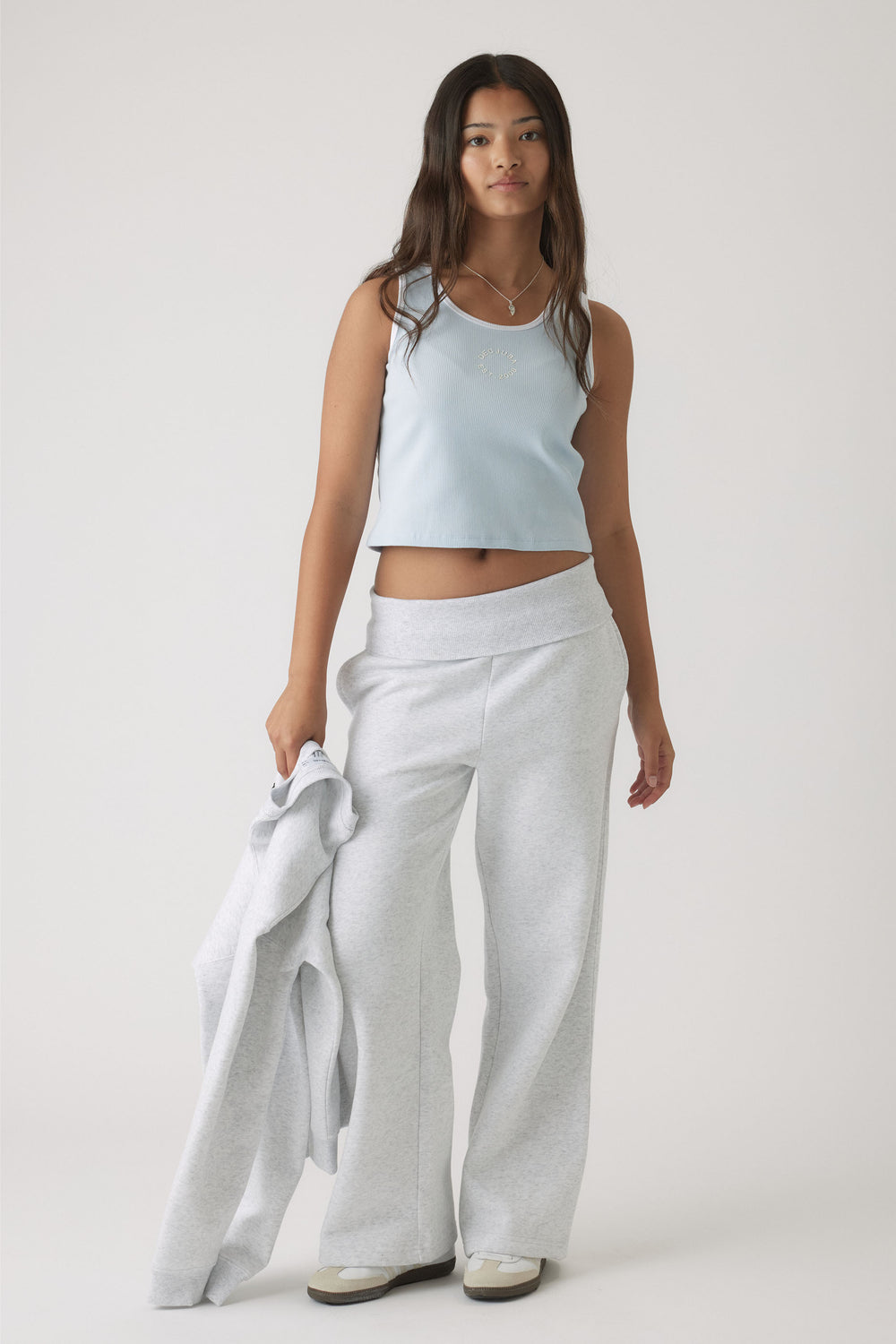 Teen girl wearing a pale blue cropped tank paired with light grey wide-leg pants, holding a matching jacket casually