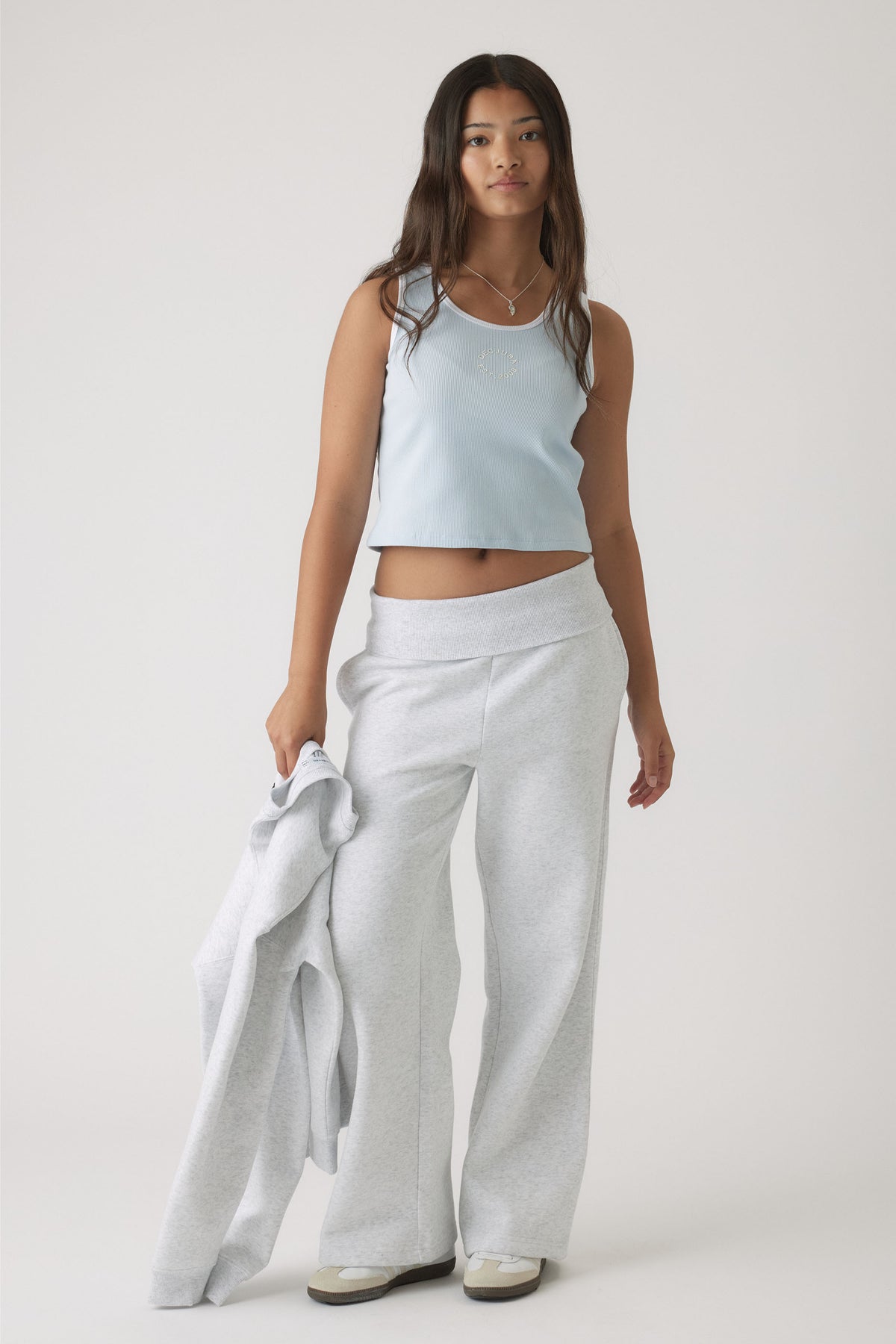 Teen girl wearing a pale blue cropped tank paired with light grey wide-leg pants, holding a matching jacket casually