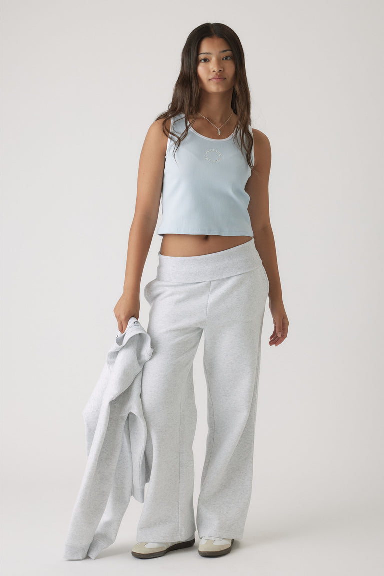 Teen girl wearing a pale blue cropped tank paired with light grey wide-leg pants, holding a matching jacket casually