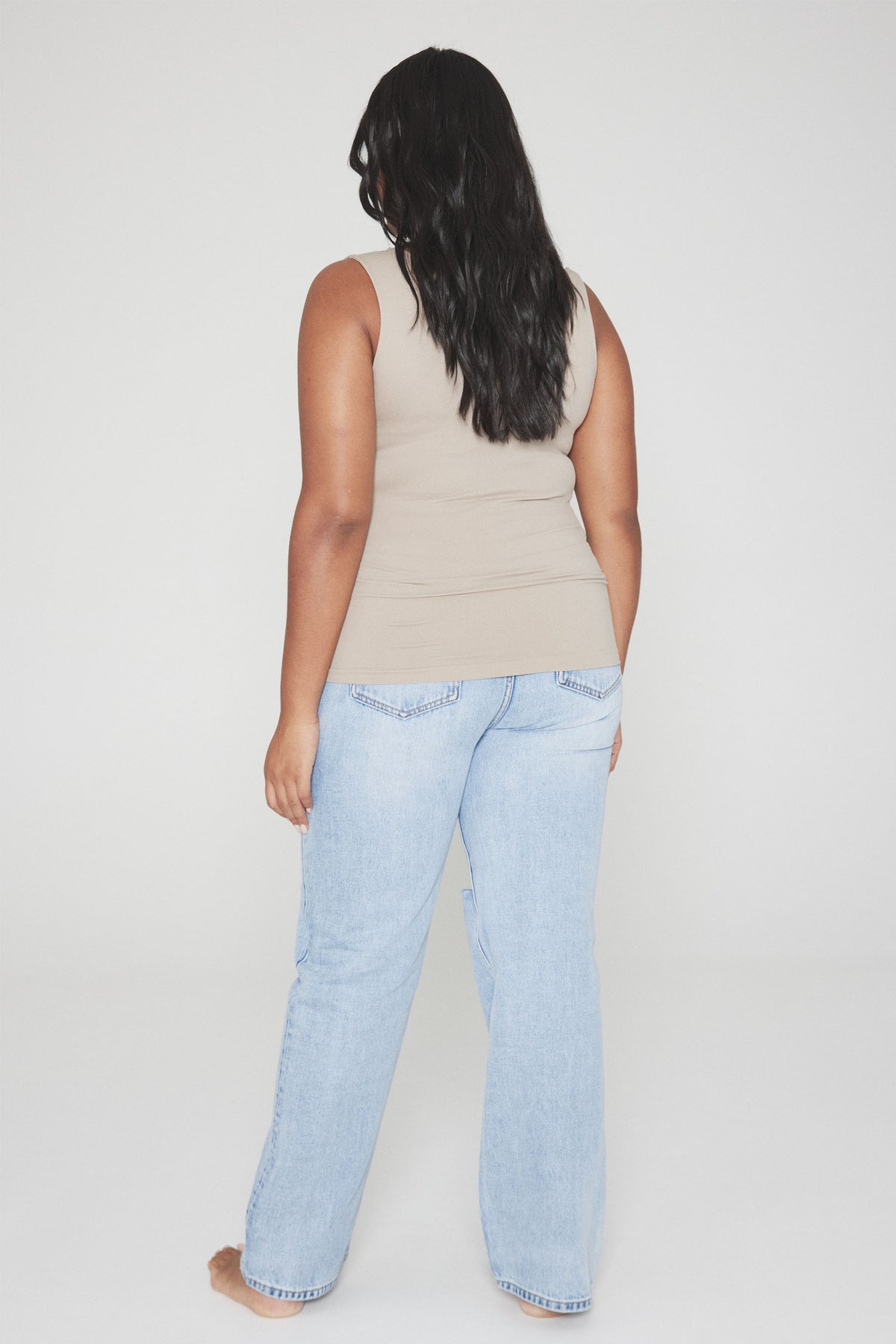 Woman wearing a beige fitted tank top with light blue wide leg jeans, back view