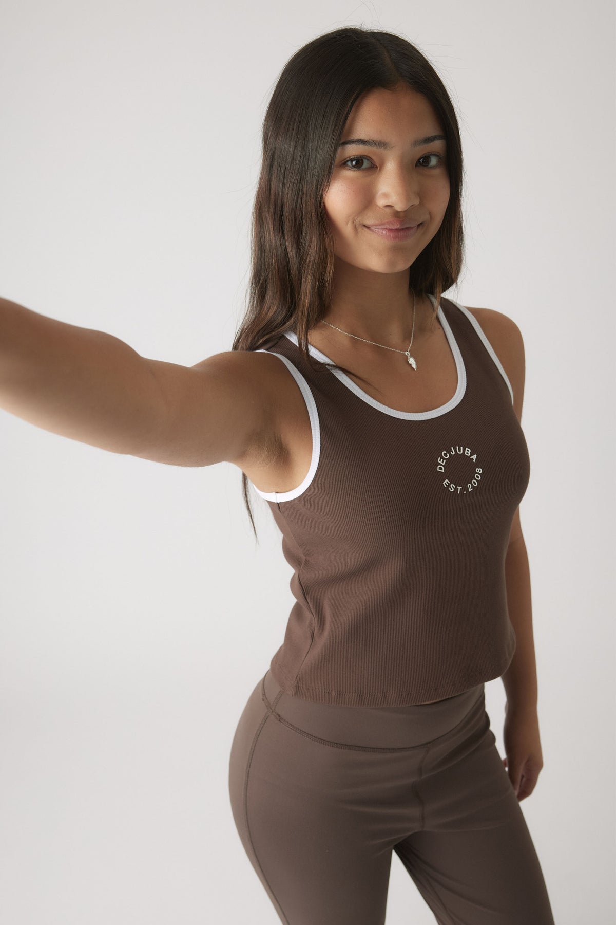 Girl wearing a mocha cropped tank with white trim paired with matching fitted leggings, smiling and posing against a white background