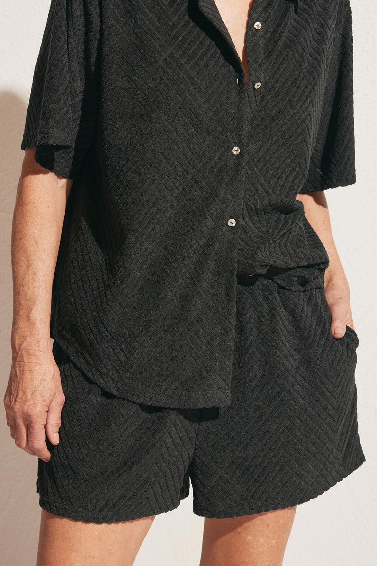 Woman wearing textured black terry shorts with a relaxed matching button-up top and pockets for casual style