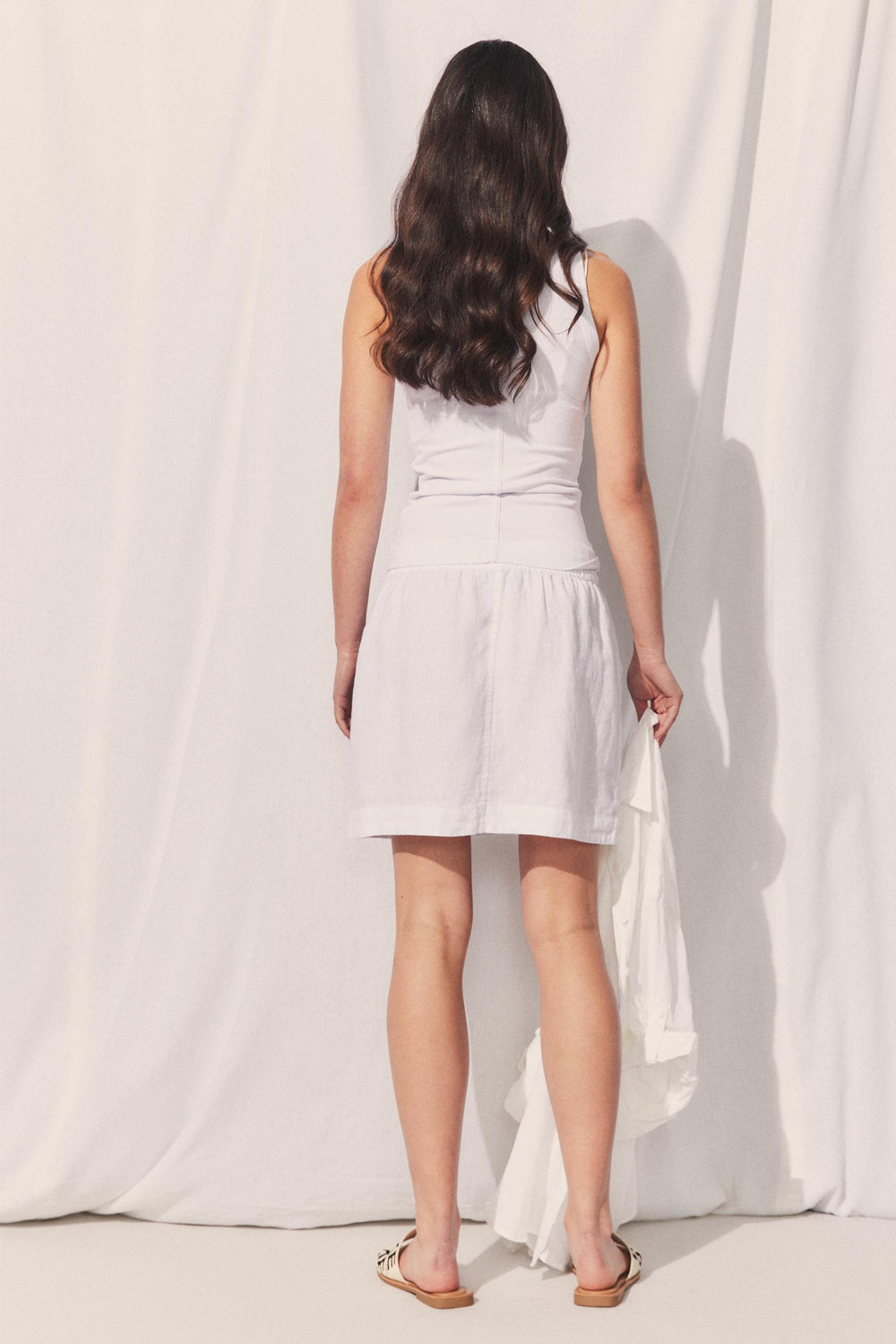 Woman seen from back wearing D-Luxe Linen Mini Skirt in gallery position 3 with soft fabric background in portrait view