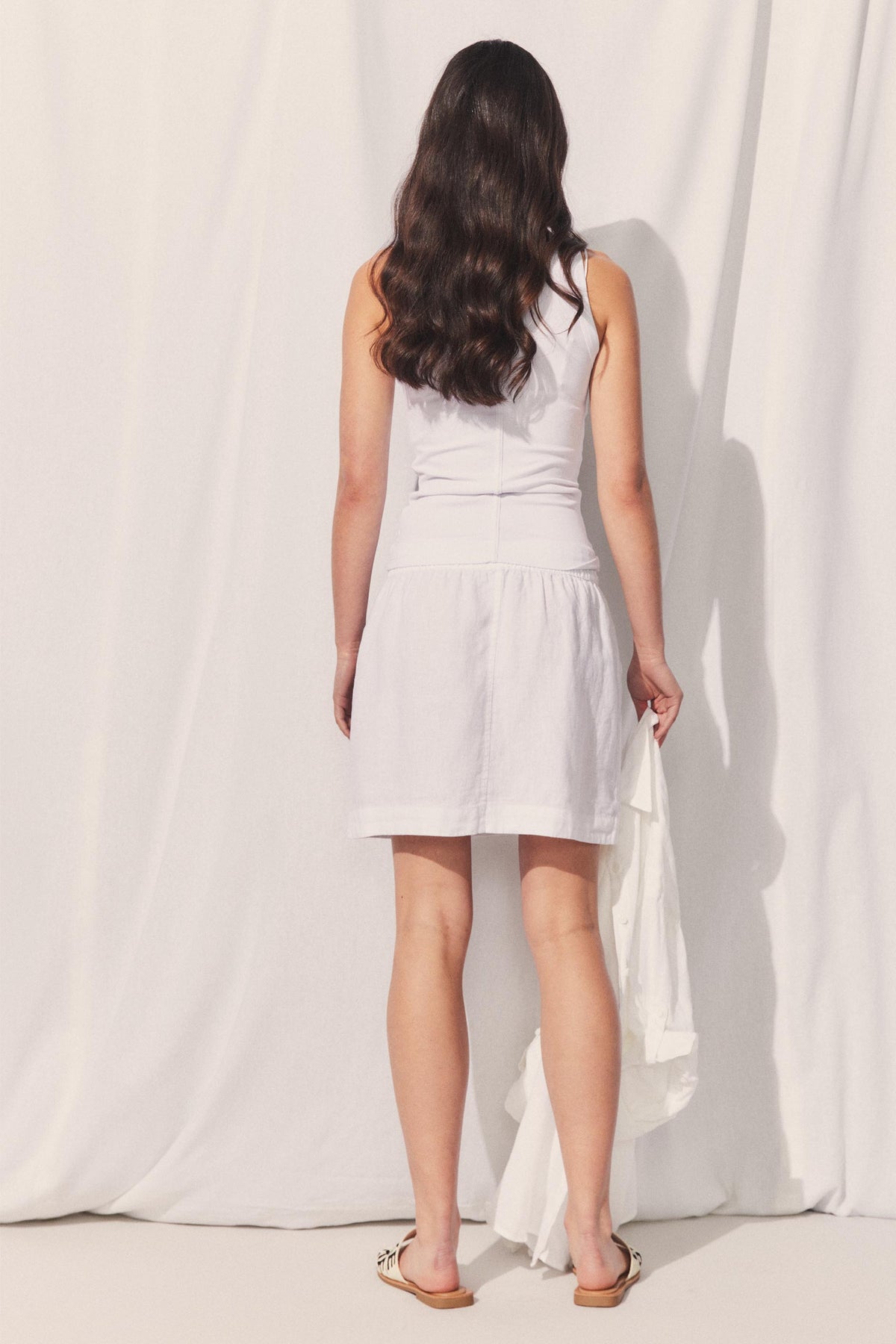 Woman seen from back wearing D-Luxe Linen Mini Skirt in gallery position 3 with soft fabric background in portrait view