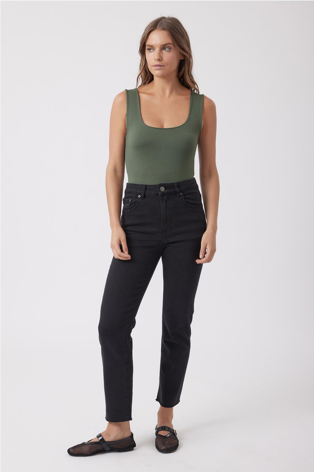 Woman wearing a green scoop neck tank top with black jeans and flat sandals
