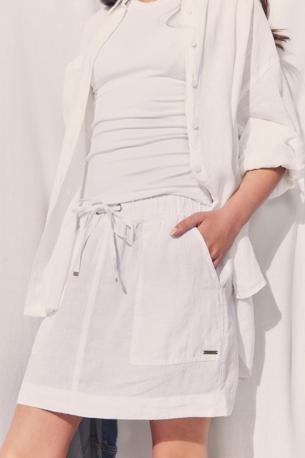 Woman wearing a white D-Luxe Linen Mini Skirt with drawstring waist and pockets, styled with a white shirt, gallery position 2.