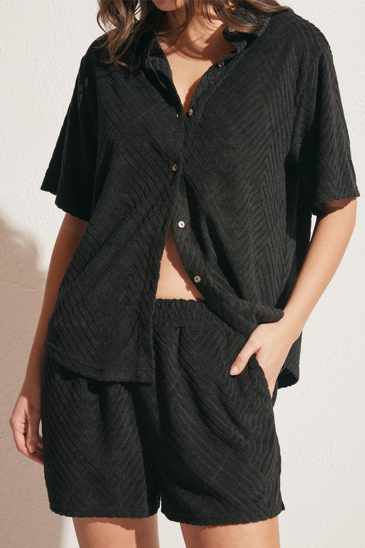 Woman wearing relaxed black textured shorts with matching short-sleeve button-up shirt in soft fabric