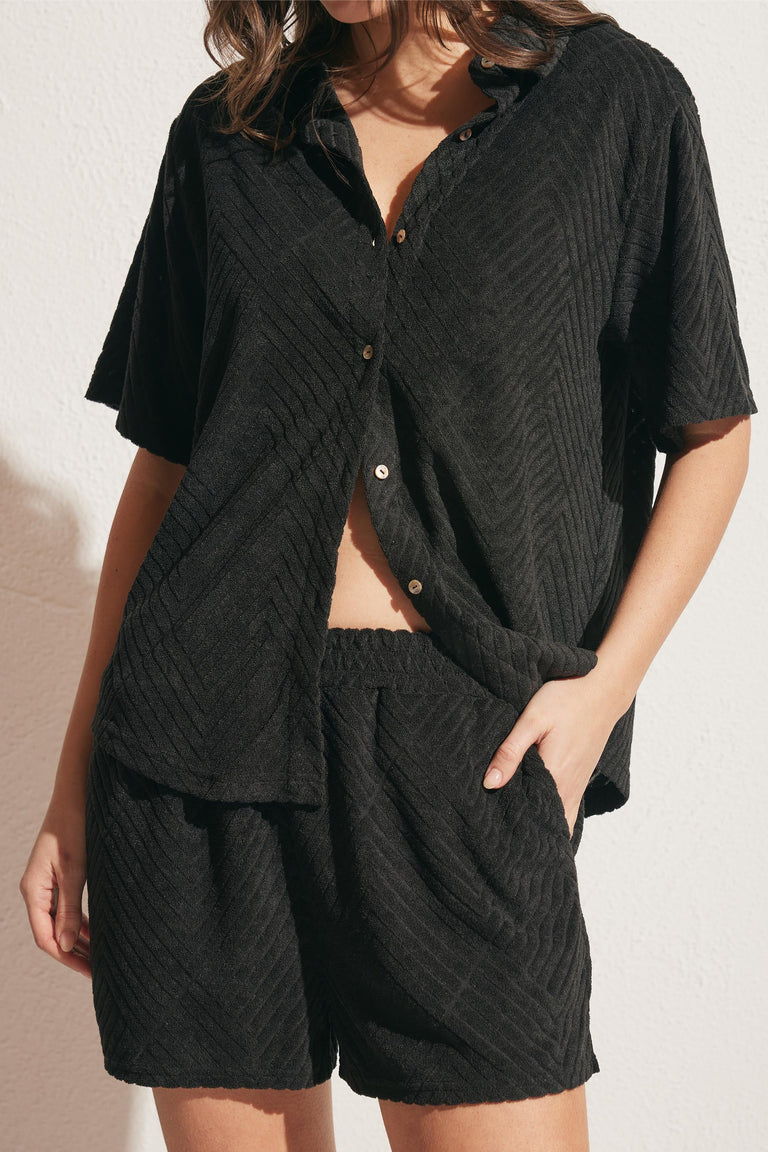 Woman wearing relaxed black textured shorts with matching short-sleeve button-up shirt in soft fabric