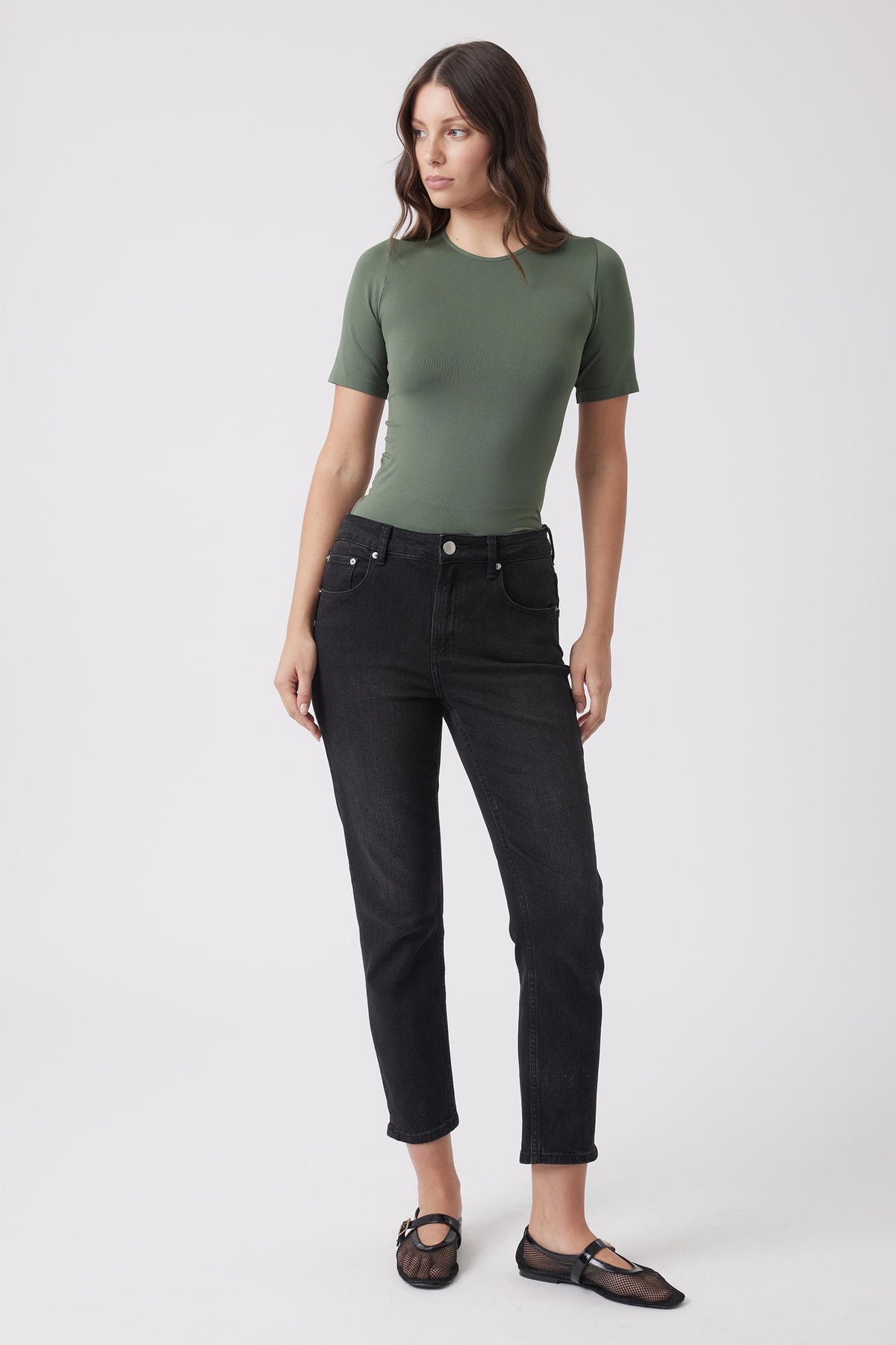 Woman wearing a fitted olive green seamless tee paired with high-rise black denim jeans and sheer black flats