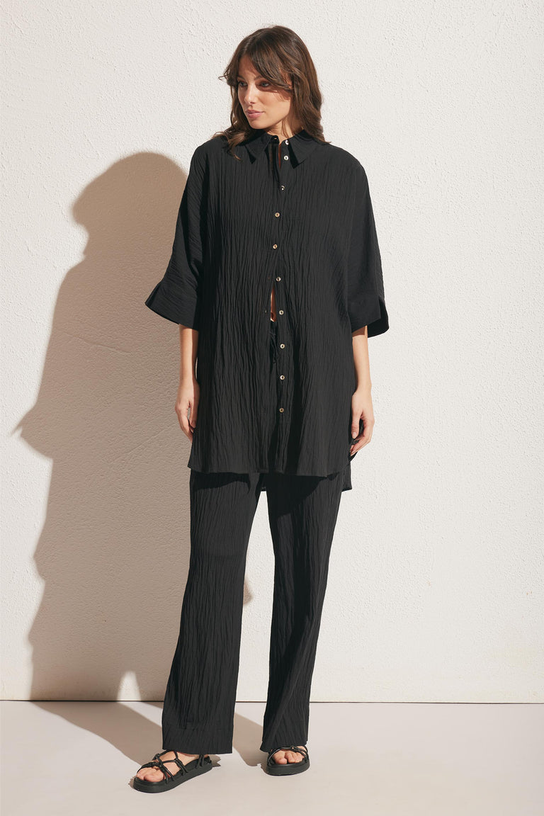 Woman wearing textured black wide-leg pants paired with a matching button-up shirt and black sandals