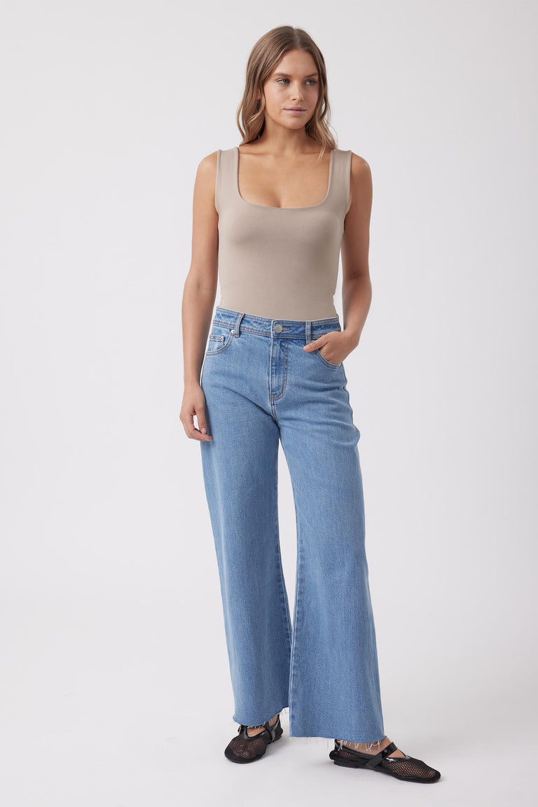 Woman wearing a taupe seamless scoop neck tank with wide leg blue jeans and black shoes