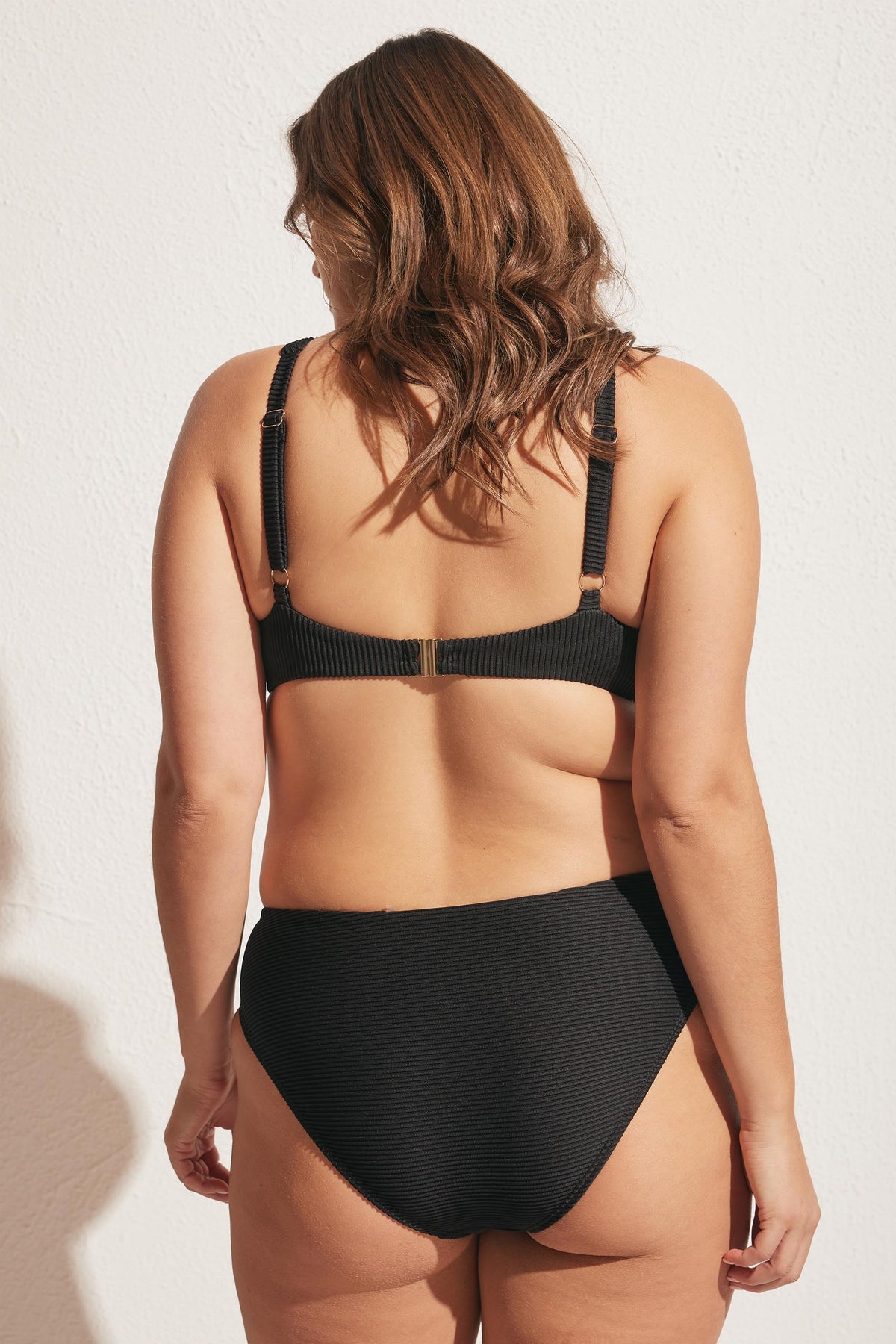 Woman wearing a black ribbed bikini top with underwire and matching high-rise bottoms, shown from the back outdoors