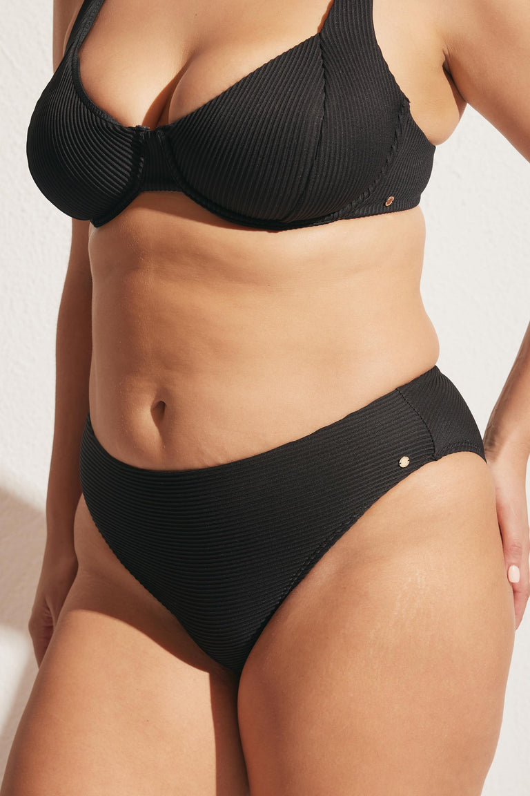 Close-up of a woman wearing a black ribbed underwire bikini top and matching high-cut bottoms in natural light