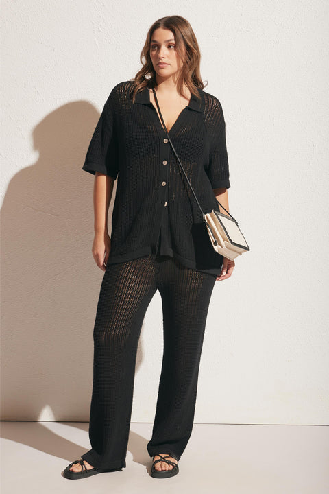 Woman wearing a relaxed black crochet button-up top and matching wide-leg crochet pants with sandals and a crossbody bag