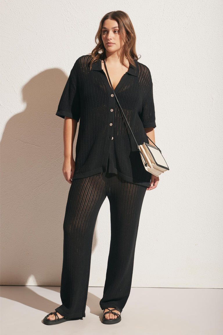 Woman wearing a relaxed black crochet button-up top and matching wide-leg crochet pants with sandals and a crossbody bag