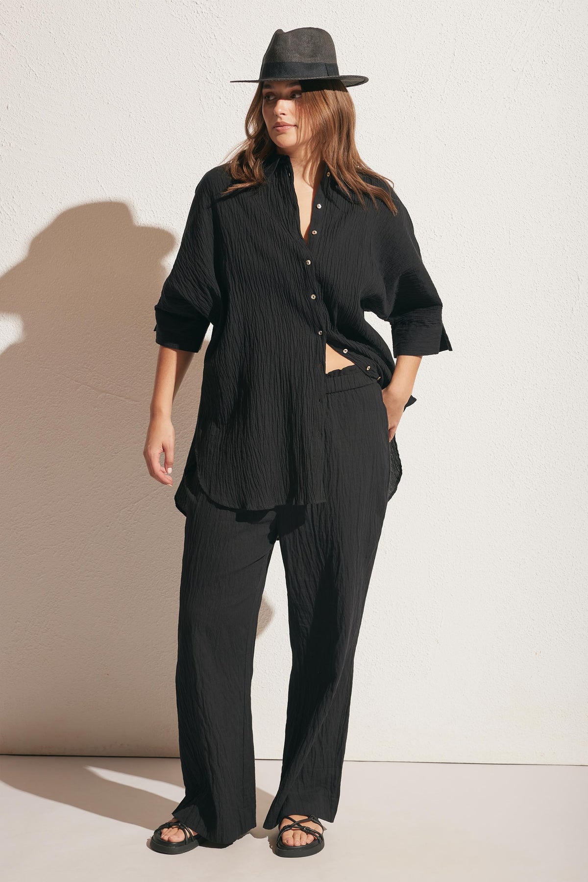 Woman wearing relaxed black textured pants paired with a loose matching long-sleeve shirt and a wide-brim hat
