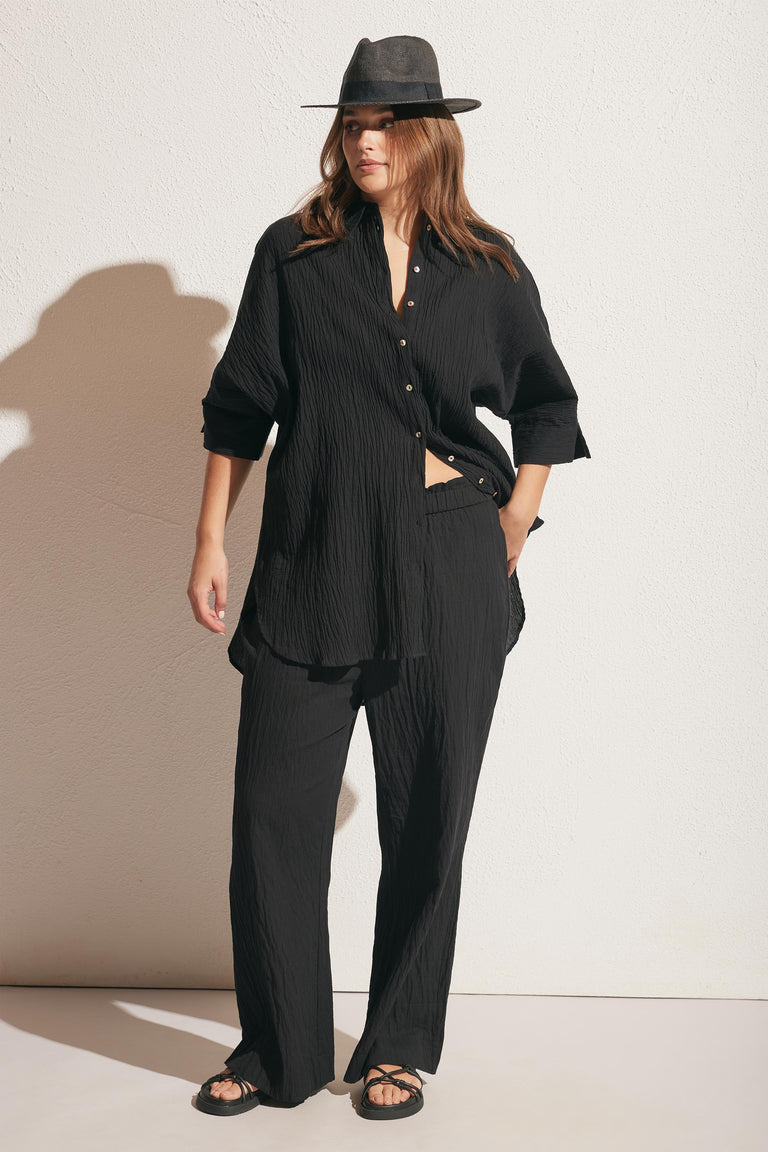Woman wearing relaxed black textured pants paired with a loose matching long-sleeve shirt and a wide-brim hat