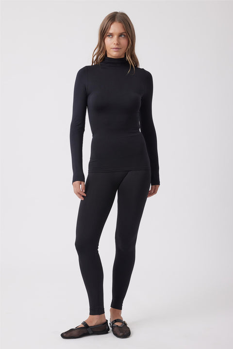 Woman wearing fitted black seamless leggings and matching long-sleeve turtleneck top with mesh ballet flats.