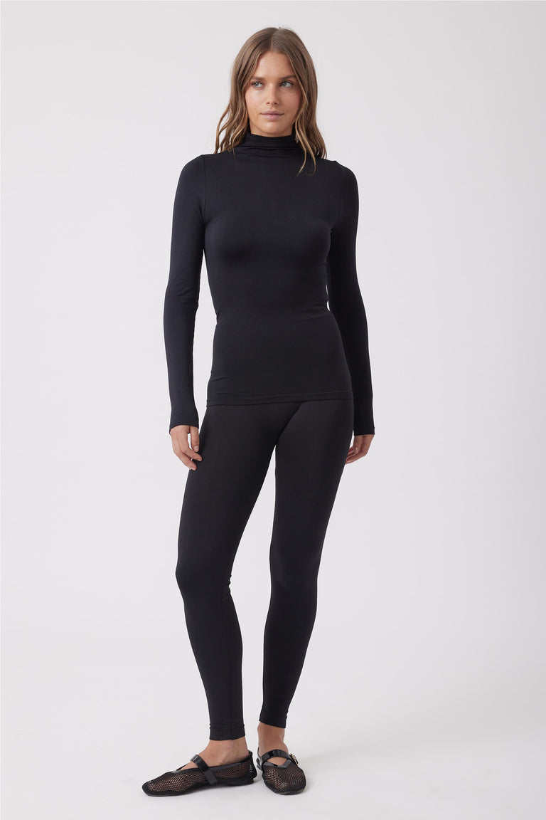 Woman wearing fitted black seamless leggings and matching long-sleeve turtleneck top with mesh ballet flats.