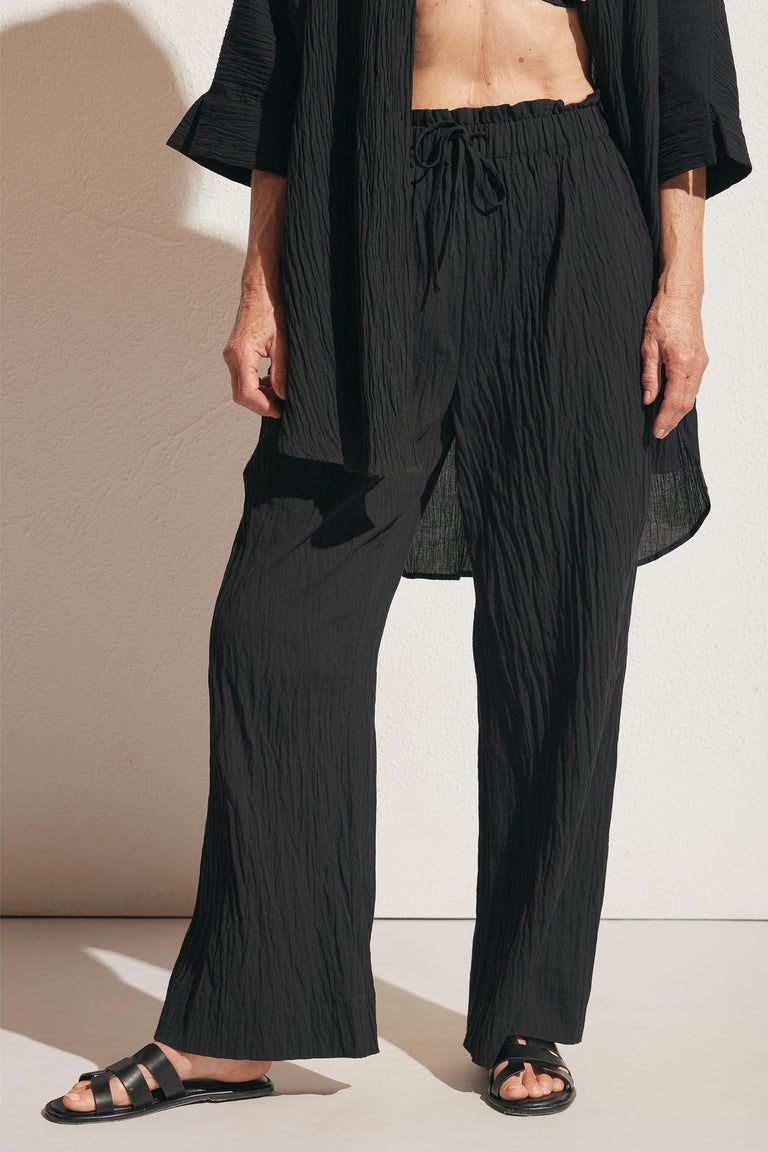 Close-up of relaxed-fit black textured pants with a drawstring waist paired with matching loose top and black sandals
