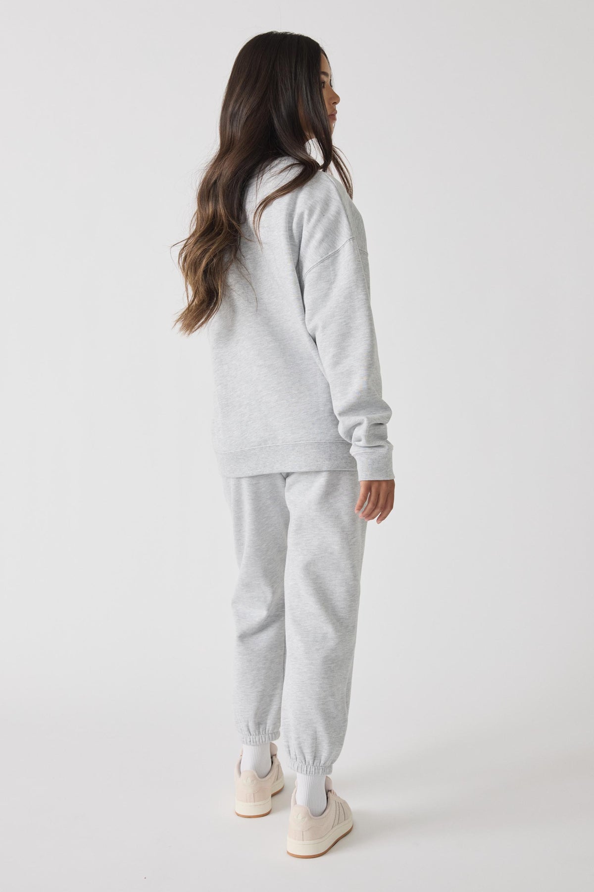 Side view of a girl wearing light grey trackpants and a matching oversized sweatshirt with white sneakers