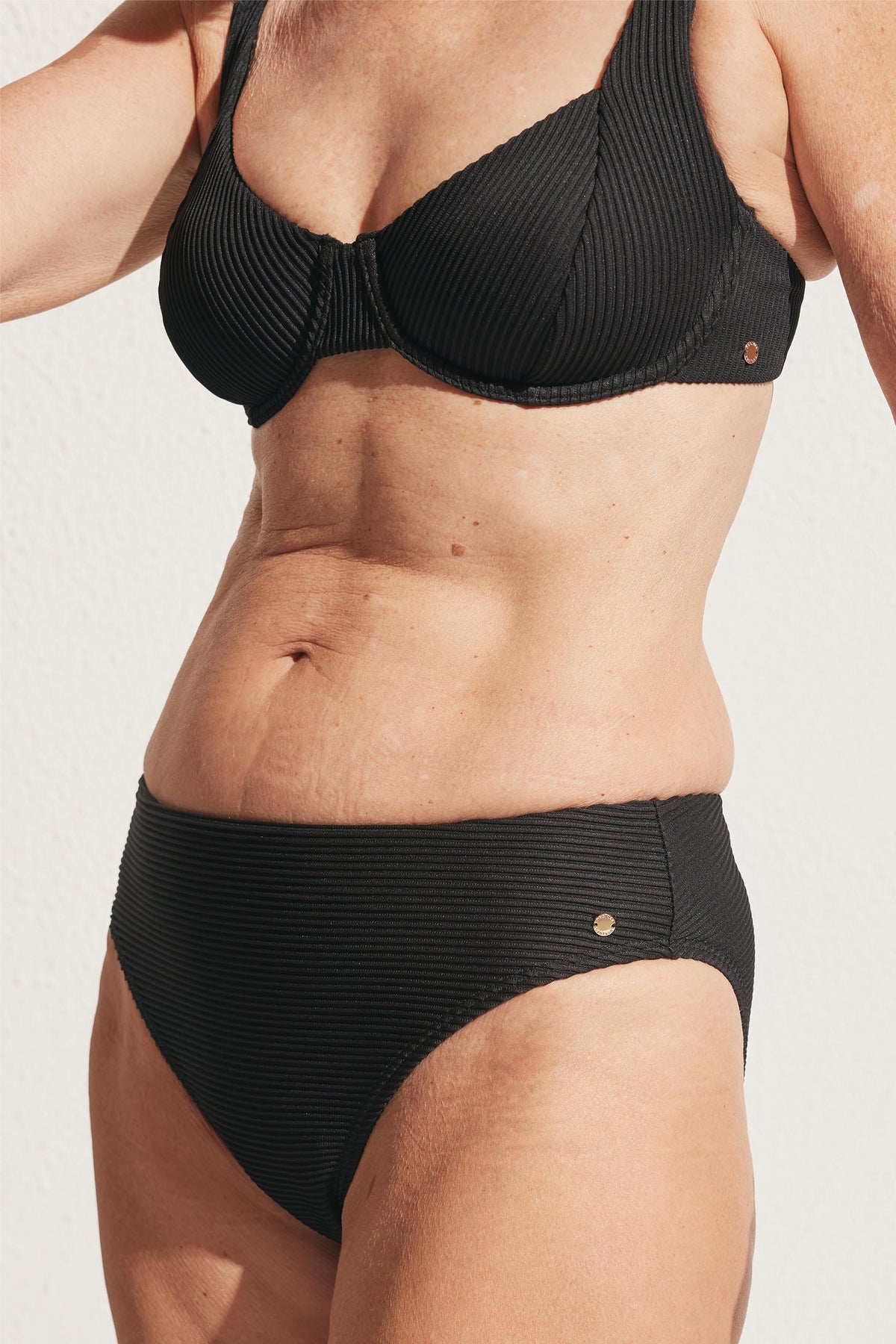 Close-up of a woman wearing a black ribbed underwire bikini top and high-waisted bottoms in natural light.