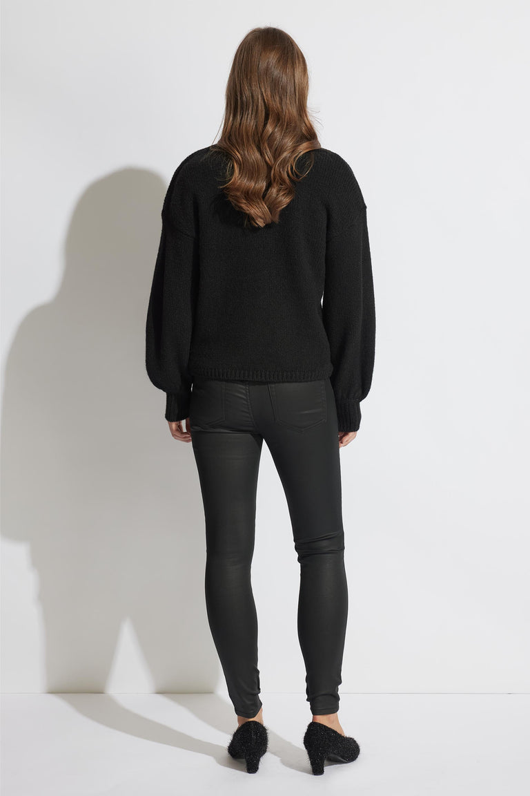 Woman wearing black coated skinny jeans paired with a cozy black sweater and textured black heels, shown from behind.