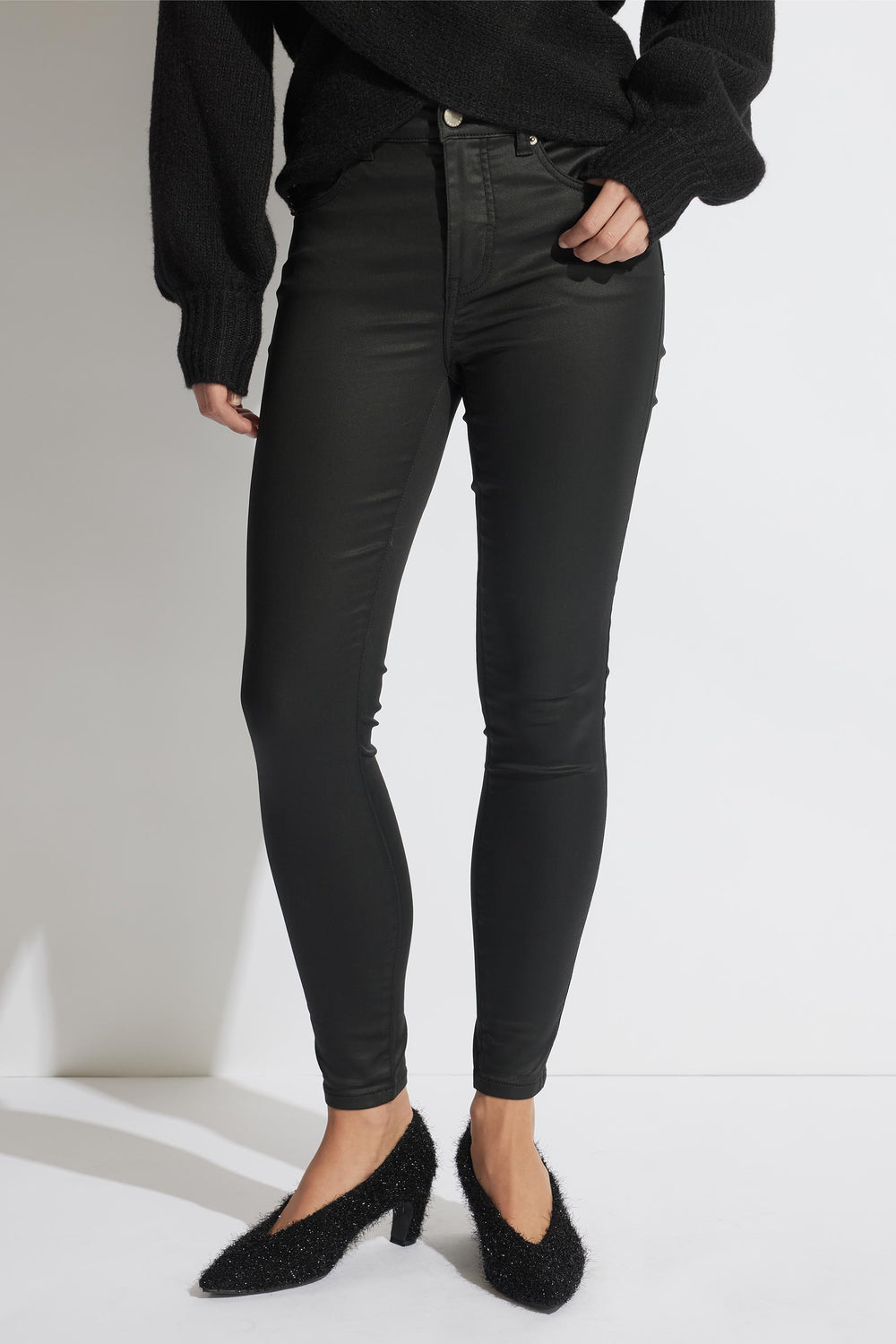 Woman wearing coated black skinny jeans paired with a textured black sweater and fuzzy pointed heels.