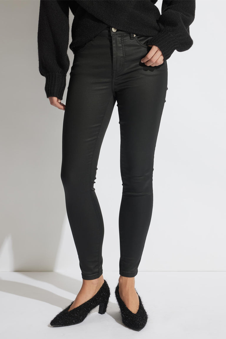 Woman wearing coated black skinny jeans paired with a textured black sweater and fuzzy pointed heels.