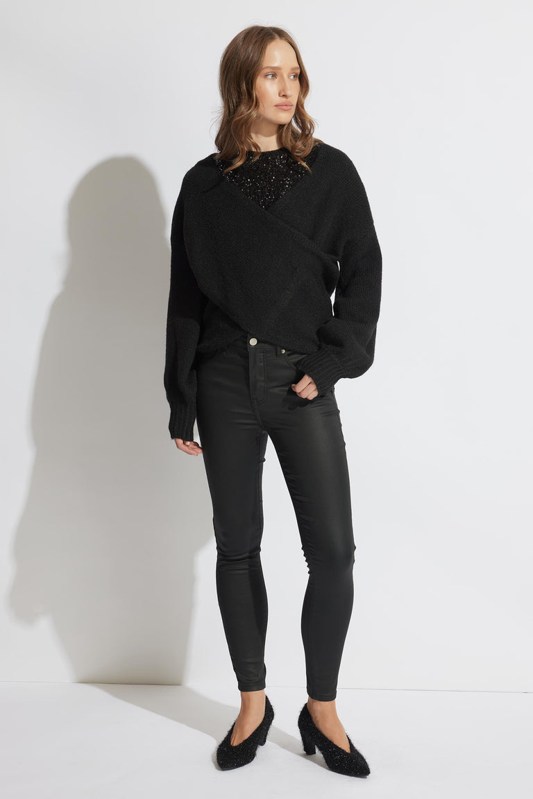 Woman wearing coated black skinny jeans paired with a textured black sweater and pointed low-heel shoes.