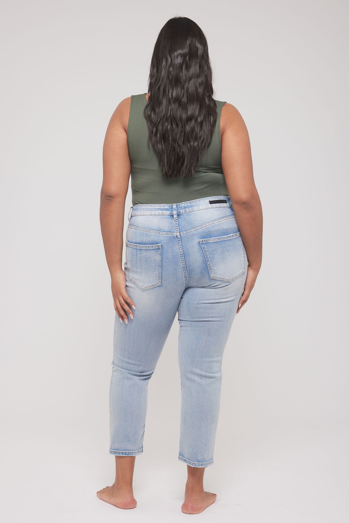 Woman wearing a fitted green sleeveless scoop tank and light wash jeans, viewed from behind