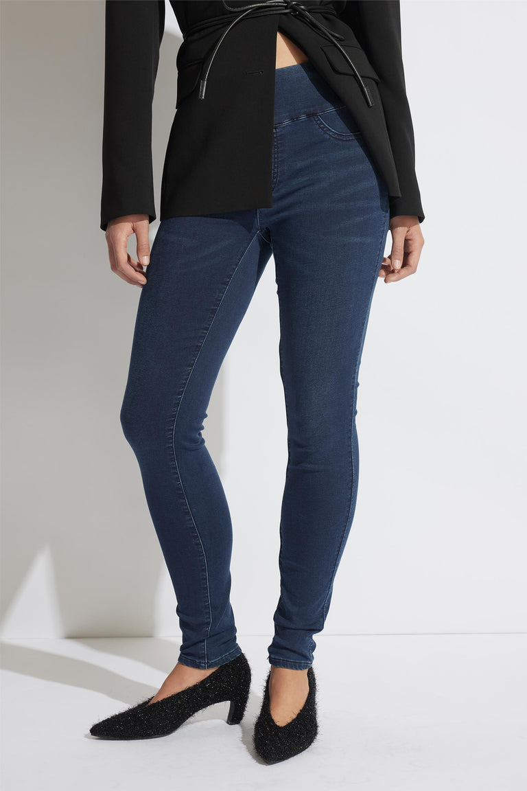 Woman wearing dark indigo skinny jeans paired with a tailored black blazer and textured black heels against a minimalist background