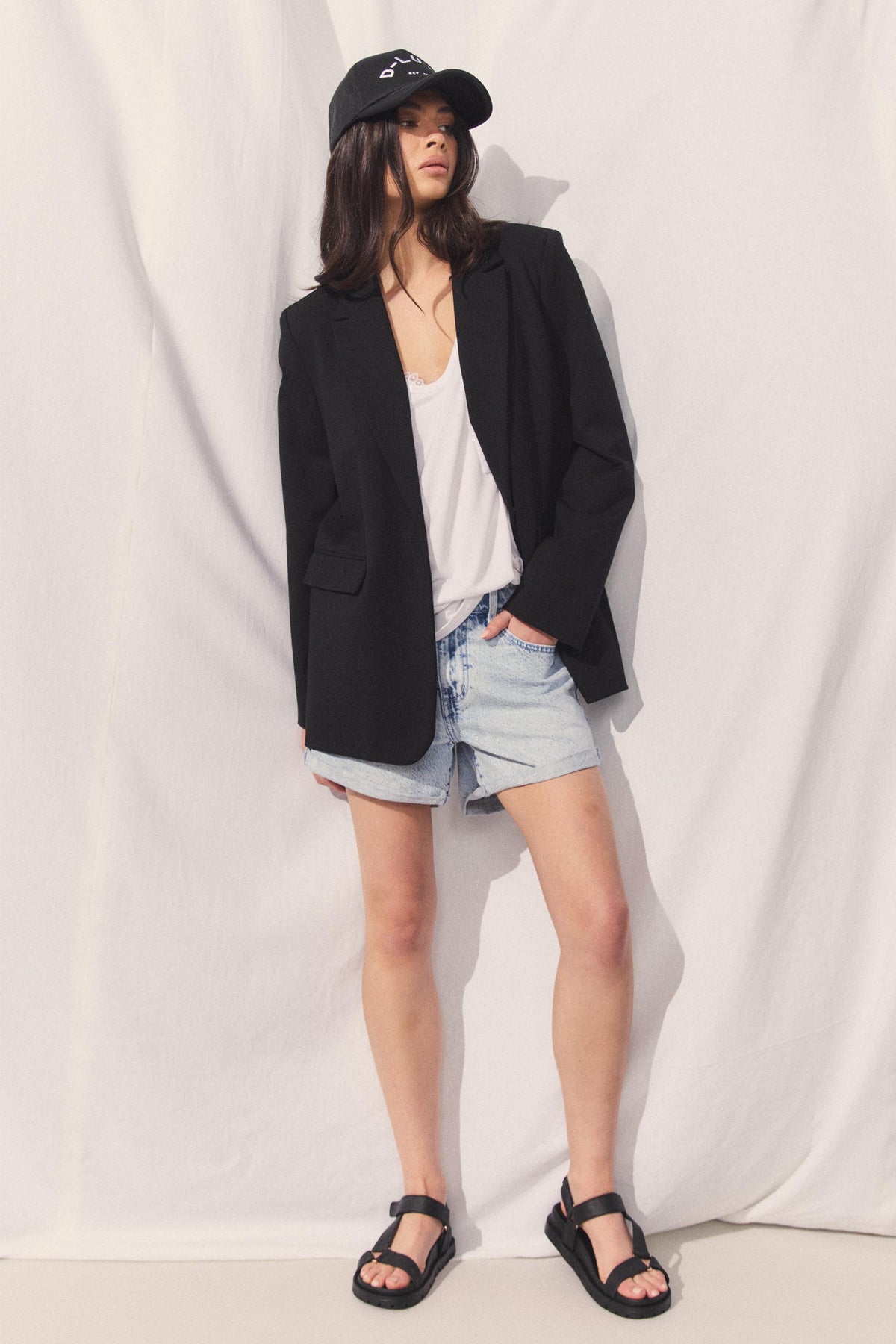Model wearing rolled cuff denim shorts with a black blazer white top and cap