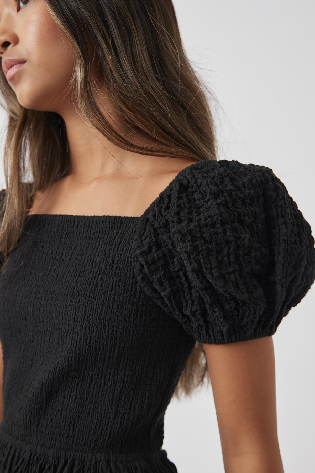 Close-up of a girl wearing a black textured mini dress with voluminous puff sleeves and a square neckline.