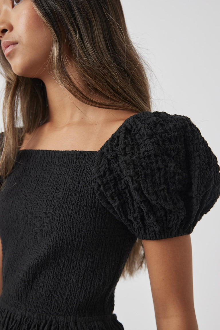 Close-up of a girl wearing a black textured mini dress with voluminous puff sleeves and a square neckline.
