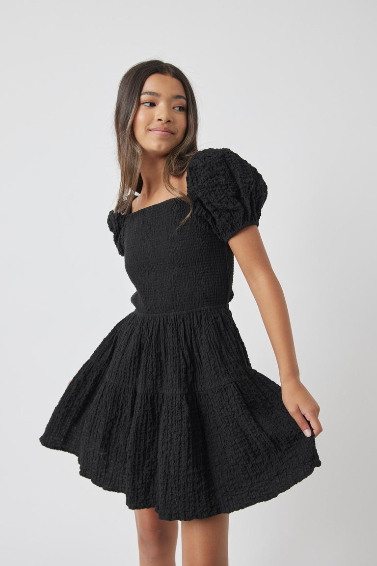 Girl twirling in textured black Girls Maude Mini Dress with puff sleeves by Decjuba Australian fashion brand
